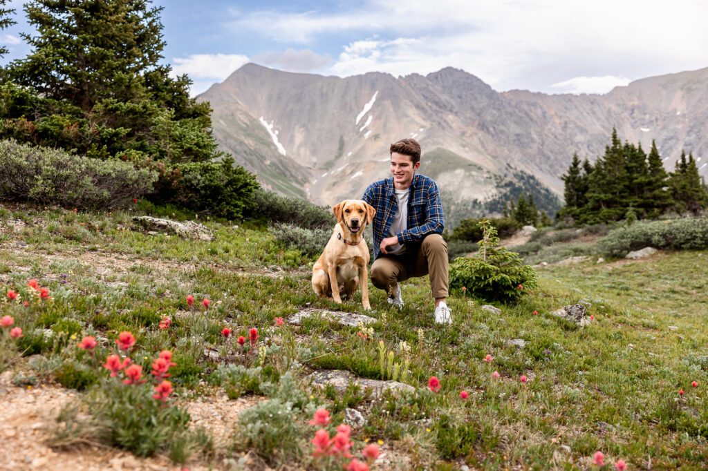 Senior pictures at Pass Lake with Colorado Lifestyle Photography with senior boy and his dog surrounded by wildflowers.
