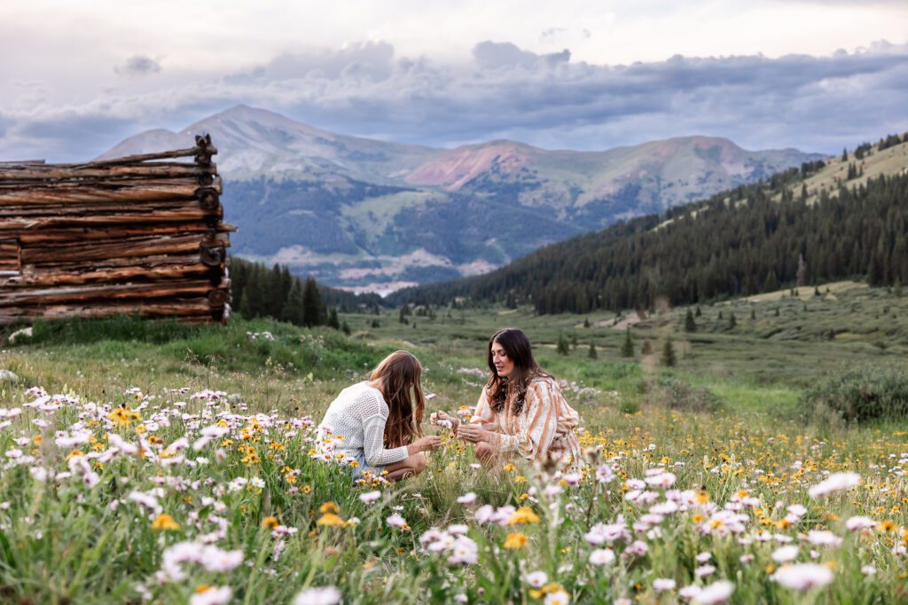 Mother and daughter picking wildflowers blooming in alpine meadow at Mayflower Gulch near Breckenridge with the Tenmile Range in the background.
